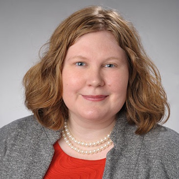 Portrait of a person with red hair wearing a red shirt and pearl necklace