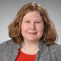 Portrait of a person with red hair wearing a red shirt and pearl necklace