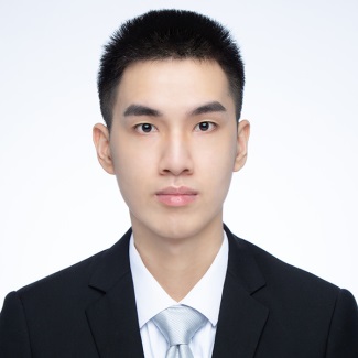 A formal portrait of a person wearing a black suit, white shirt, and looking directly at the camera with a neutral expression. The background is plain white.