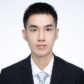 A formal portrait of a person wearing a black suit, white shirt, and looking directly at the camera with a neutral expression. The background is plain white.