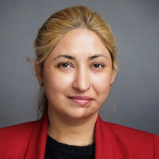 A person with blond hair pulled back wearing a red blazer with a black shirt.
