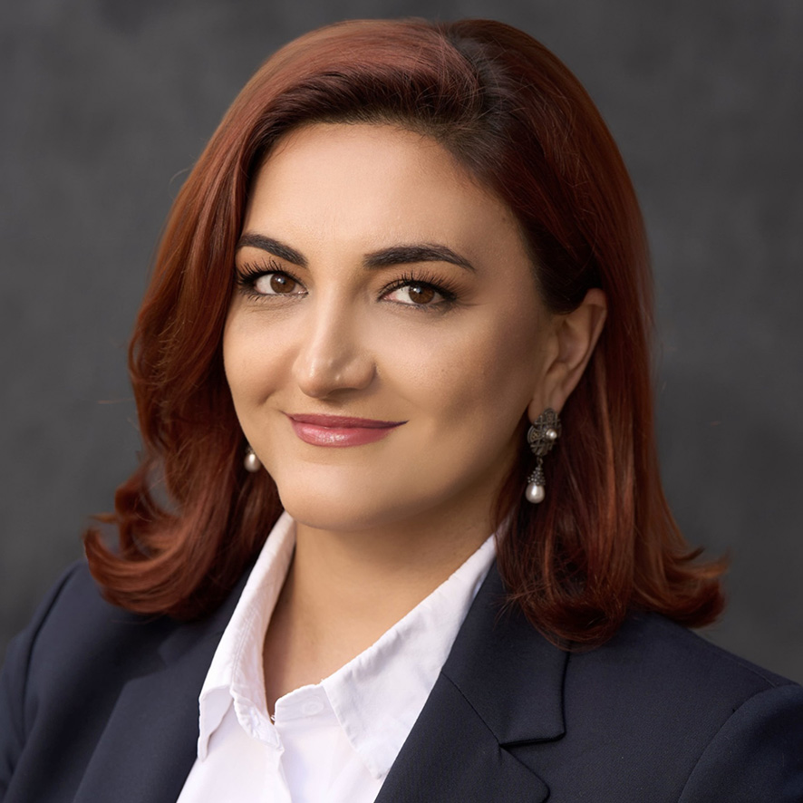 Professional headshot of a person with shoulder-length auburn hair, wearing a dark blazer and a white shirt.