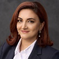 Professional headshot of a person with shoulder-length auburn hair, wearing a dark blazer and a white shirt.
