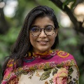 Photo of a young woman with dark hair, glasses and a colorful top.