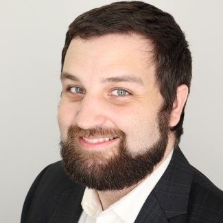 Portrait of a smiling person with a beard, wearing a suit jacket and white shirt.