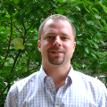 Photo of a man standing in front of trees.