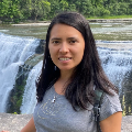 Photo of a person with long hair in front of a waterfall.