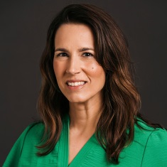 Portrait of a person smiling, wearing a green top, against a dark gray background.
