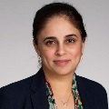 Portrait of an individual wearing a dark blazer and a patterned scarf, with a subtle smile.