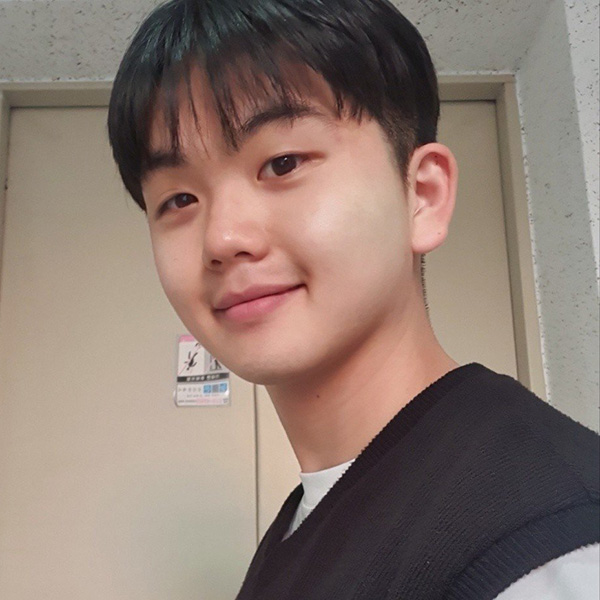 A person with short dark hair, smiling, wearing a dark sweater vest indoors.