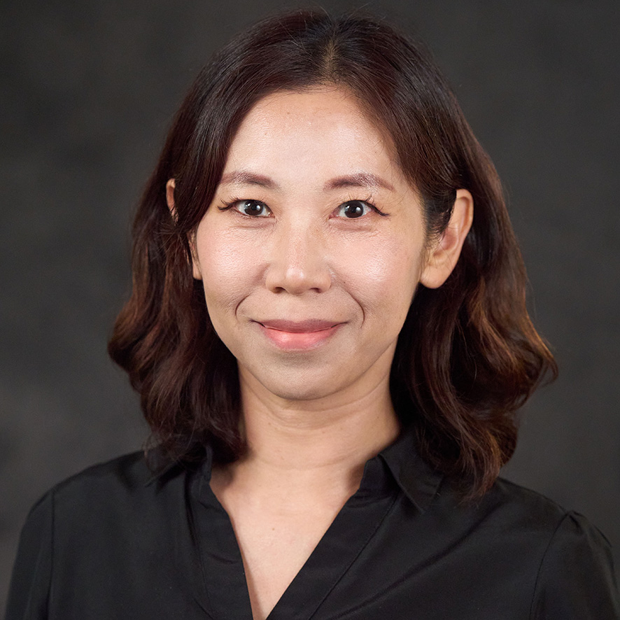Portrait of a smiling individual with shoulder-length hair, wearing a black shirt, set against a dark background.
