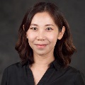 Portrait of a smiling individual with shoulder-length hair, wearing a black shirt, set against a dark background.