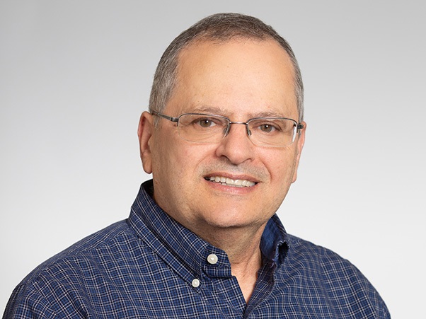 A person with short hair, wearing glasses and a blue button down shirt.