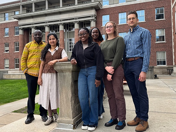 Six public health researchers posing together outside brick campus building.