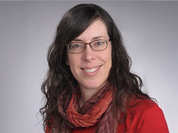 A amiling person with long dark hair wearing glasses, a red top and a patterned scarf.