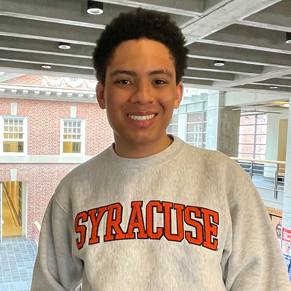 A person with dark hair, smiling and wearing a Syracuse sweatshirt.