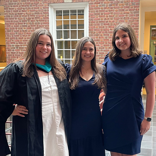 Three people in commencement attire pose together in a brick courtyard.